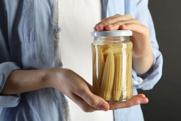 Woman with jar of tasty pickled yellow baby corns on gray background, closeup