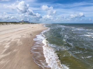 Aerial photo of Kijkduin beach under a partly cloudy sky with a few people walking along the sandy beach.