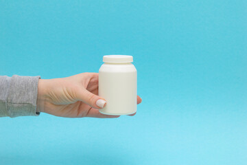 the pill bottle, medicine container for vitamins in female hand on blue background.