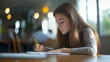 © forenna - Side profile of a focused young teenage girl holding a pencil while taking an exam. The image captures a diligent college or high school student sitting at a table, writing on a pa