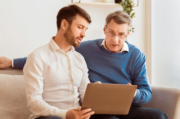 Poster - Mature Son Teaching Senior Father To Use Laptop Computer And Internet Sitting Together On Sofa At Home. Selective Focus