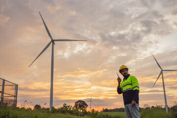 Wall Mural - man in a yellow and black safety vest stands in front of two wind turbines