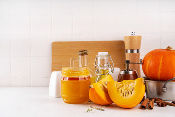 Wall Mural - Pumpkins cooking background with sliced and whole pumpkin halves or butternut squash, raw herbs. spices on white background with cutting board, herbs, honey. Thanksgiving dinner seasonal cooking