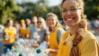 © LifeMedia - A cheerful volunteer wearing an apron and glasses helps distribute bottled water at a charity event with a group of other volunteers in the background on a sunny day.