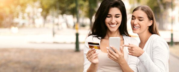 Poster - Online payment and e-banking. Close female friends holding credit card and mobile shopping application outdoor