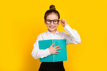 Wall Mural - Photo of cute schoolgirl touch eyeglasses hold book wear uniform isolated on yellow color background