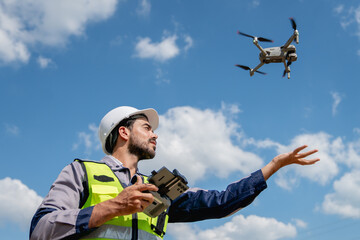 Engineer in a safety vest operating a drone to inspect and survey electrical power lines. Technician inspecting the power station for scheduled maintenance.