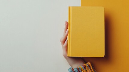 Poster - Young Womans Hand Holding Vibrant Orange Notebook in Soft White Minimalistic Background, Daytime, Advertising & Commercial