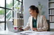 © Crystal - Young asian businesswoman smiling and working on a laptop, calculating financial data at her office desk