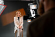 © Big Shot Theory - A professional woman wearing a business suit is being filmed in a studio setting