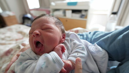 Newborn baby nestled in mother's embrace, eyes closed, wearing a cute blue onesie, experiencing a peaceful nap in the comfort of home, symbolizing love and care