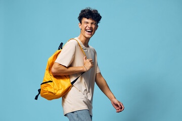 Wall Mural - Young man smiling with a yellow backpack on a blue background, exuding happiness and energy, ideal for travel or lifestyle concepts