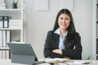 © Crystal - Asian businesswoman is smiling while sitting at her desk with her arms crossed in her office