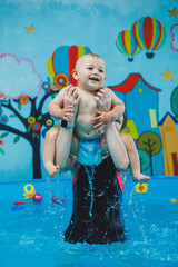 Wall Mural - A trainer teaches a little boy to swim in a children's pool. Courses for teaching swimming to babies.