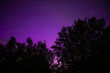 night starry sky outside the city with purple reflections of the northern lights
