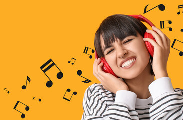 Stylish young woman in headphones with nose piercing on yellow background