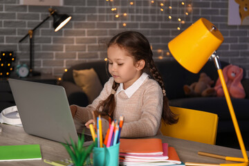 Wall Mural - Little girl with laptop doing lessons at home late in evening