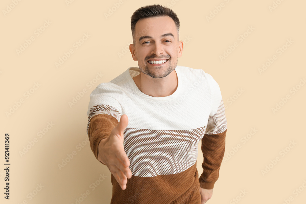 Happy young man reaching out for handshake on beige background