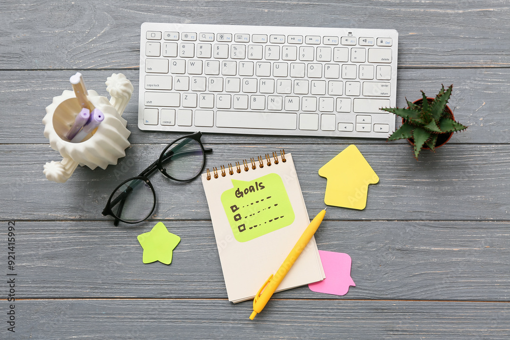 Sticky notes with to do list, computer keyboard and notebook on black wooden background. New year goals concept