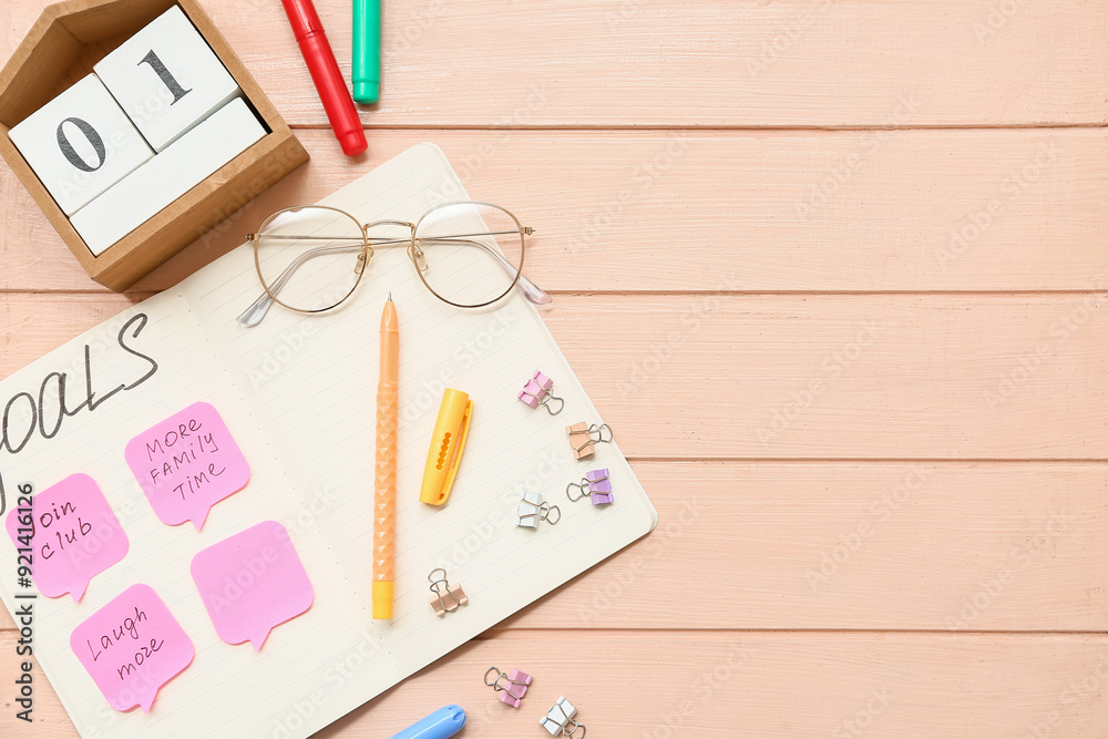 Notebook with to do list, calendar and sticky notes on beige wooden background. New year goals concept
