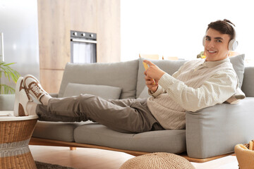 Wall Mural - Young man in headphones using mobile phone on sofa at home