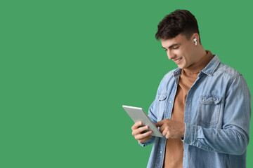 Young man in earphones using tablet computer on green background