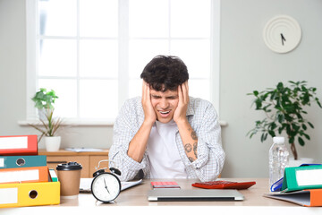 Wall Mural - Frustrated male accountant sitting at workplace with folders and alarm clock in office