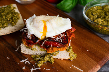 Wall Mural - Poached Egg Sandwich with Fried Prosciutto and Tomatoes: Breakfast sandwich with soft egg, prosciutto and plum tomatoes on a ciabatta roll with pesto