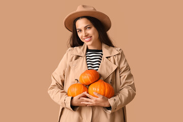 Sticker - Stylish young woman with fresh pumpkins on brown background