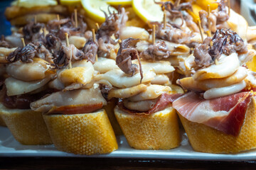 Typical snacks of Basque Country, pinchos or pinxtos skewers with small pieces of bread, fish, sea food, sweet green pepper served in bar in San-Sebastian or Bilbao, Spain