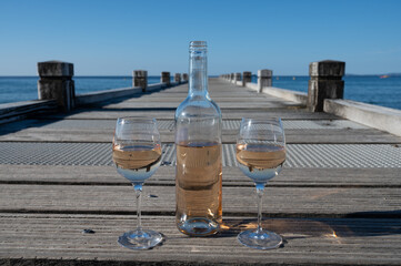 Tasting of cold rose wine from Provence outdoor on wooden yacht pier with view on blue water and white sandy beach Plage de Pampelonne near Saint-Tropez, summer vacation in France