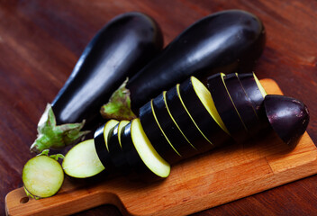 Sticker - Closeup of fresh eggplants with chopped slices on wooden surface. Healthy vegetarian ingredient