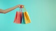 © Watasiwa - Hand holding colorful shopping bags against a blue background