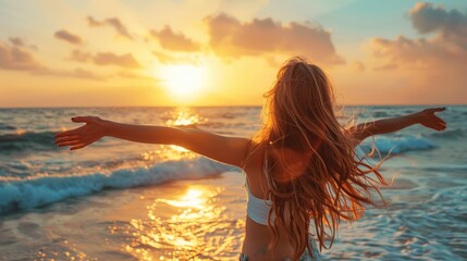 Wall Mural - Woman standing on beach with arms outstretched at sunset.