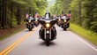 © Mont - A group of motorcycles rides down a scenic road, showcasing American pride with flags flying in the breeze amidst lush greenery.