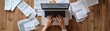 © Mont - Aerial view of hands typing on a laptop surrounded by paperwork, symbolizing productivity and organization in a workspace.