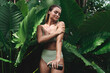 © blackday - Young woman applying body lotion  surrounded by lush tropical leaves