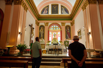 Two men praying in a beautifully adorned church interior with religious statues and paintings