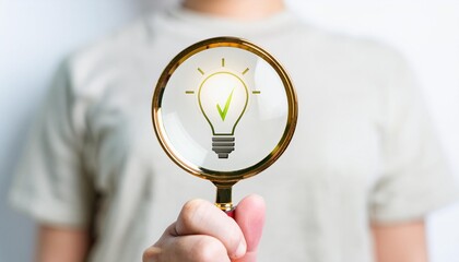 A hand holding a magnifying glass with a light bulb icon inside, symbolizing the search for ideas and solutions