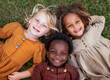 © idcreative.ddid - Closeup photo from above of three multiethnic children smiling and lying on the grass. Kids, diversity and happiness of group enjoying summer holiday at park or garden, bonding or relaxing together.