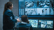 © Framestock - Female security worker talks with African American colleague, uses tablet. Multiethnic CCTV operators control security cameras on computer monitors and big digital screen with surveillance footage.