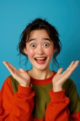 Portrait Of A Young Asian Lady Smiling With A Cheerful Expression, Showing Something Amazing In Blank Space, Wearing Casual Clothing, Looking Front, Isolated Against A Blue Wall