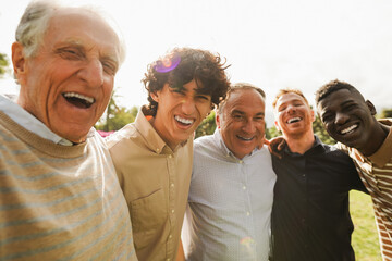 Wall Mural - Multi generational men smiling in front of camera - Male multiracial group having fun togheter outdoor - Focus on left boy face