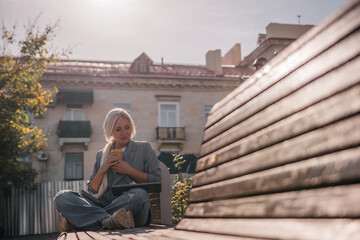 Wall Mural - A woman sitting on a bench with a cell phone in her hand. She is wearing a suit and she is working on her phone.