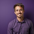 © Kakabe - A cheerful man wearing a purple shirt stands against a matching purple background, smiling at the camera great for using in casual professional settings, lifestyle blogs, or personal branding content