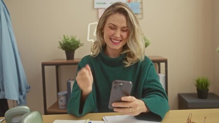 Canvas Print - A joyful blonde woman enjoys success on her smartphone at home, conveying emotion and connectivity indoors.