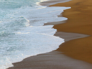 Landscape of a sand beach and blue ocean waves with white foam 