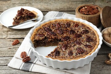 Wall Mural - Delicious pecan pie in baking dish and fresh nuts on wooden table, closeup