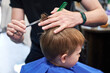 © anatoliy_gleb - Man barber cutting little boy's hair using comb and scissors. Child getting haircut from adult male, likely barber. Professional hairdresser and cute client at modern barbershop.