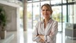 © JINGWEN - Confident businesswoman with crossed arms smiling in modern office, facing camera, embodying success in professional attire with sleek hairstyle.